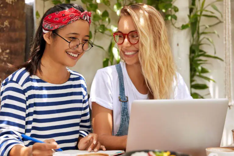 Female freelance partners get good feedback on website, look joyfully at screen of laptop computer,